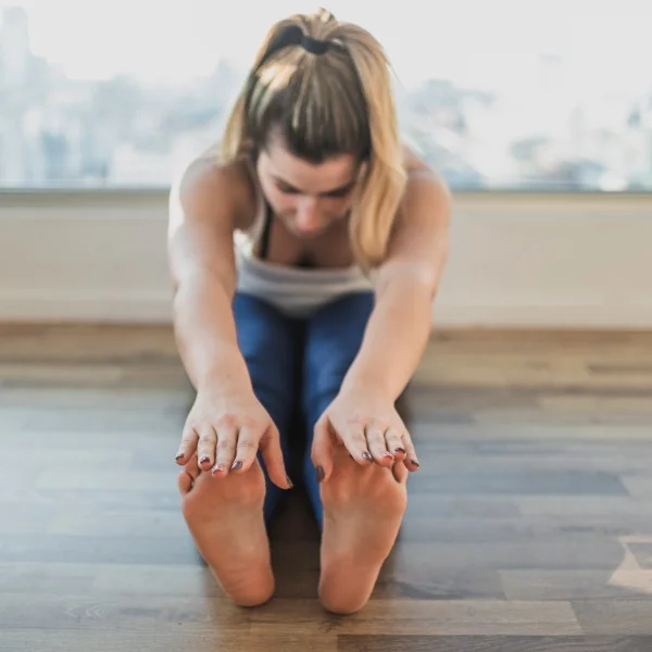 Une femme s'étire les jambes sur le sol, adoptant une posture de flexibilité et de bien-être.