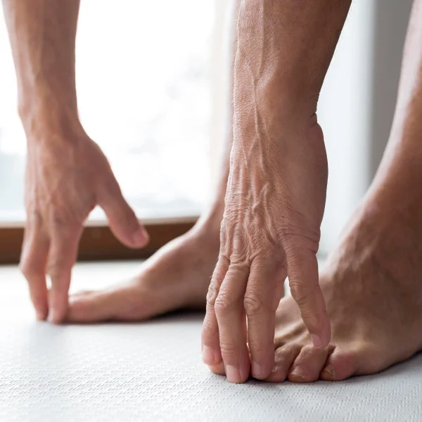 Pieds d'une personne sur un tapis, mains posées au sol, en position de yoga ou d'étirement.